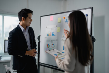 Aufkleber - Two Asian businesspeople discussing strategy and analyzing data charts on a whiteboard in an office, collaborating on a project and sharing ideas for informed decisions