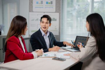 Aufkleber - Asian businesspeople engaging in discussion and brainstorming around a project, analyzing charts and graphs displayed on a laptop in a modern meeting room setting