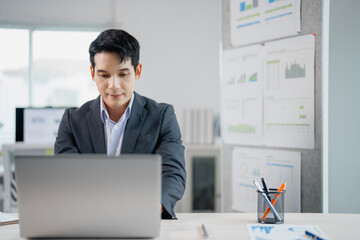 Aufkleber - Focused employee concentrating on work, typing on laptop at desk in bright office, with charts and graphs displayed on nearby board, demonstrating productivity and professionalism