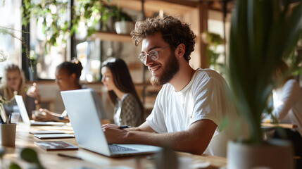 Poster - Young man working on laptop in modern coworking space during daytime surrounded by focused individuals