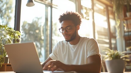 Poster - Young man working on a laptop in a bright and cozy workspace filled with plants during the day