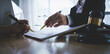 © Natthawadee - Two hands, one belonging to a legal professional, point to a document for a client to sign, with a gavel and scales of justice nearby.