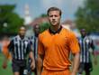 © alsu0112 - Male soccer player in bright orange uniform stands confidently on the field, surrounded by teammates in black and white uniforms, showcasing athleticism and team spirit
