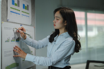 Poster - Asian businesswoman analyzing financial charts and graphs using pen, working in office