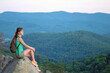 © bilanol - Sportive woman sitting alone taking a break on hillside trail. Female hiker enjoying view of nature from rocky cliff on wilderness path. Active lifestyle concept