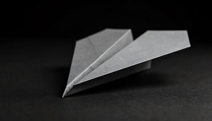 Poster - A sleek, gray paper airplane rests on a dark surface, showcasing its simple yet elegant design in a minimalist setting