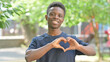 © stockbakers - Casual African Man Making a Heart Gesture Outdoors