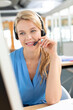 © WavebreakMediaMicro - Female call center representative handling calls at desk in open-plan office with headset