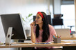 © WavebreakMediaMicro - Asian woman wearing headset and striped shirt sitting at modern office desk typing on keyboard