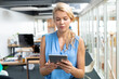 © WavebreakMediaMicro - Woman wearing sleeveless blue blouse standing and holding tablet computer in office near desks