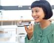 © WavebreakMediaMicro - Asian woman holding smartphone near mouth, speaking into it at desk in open-plan office, copy space
