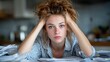 © Freshpixel - A candid shot of a young woman with wild hair, sitting amidst a chaotic pile of paperwork, expressing stress and overwhelm in a relatable way.