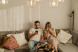 © blackday - Happy Couple Sitting Together on Sofa Using Smartphone and Drinking Coffee