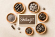 © KRISTINA KUPTSEVICH - Various Forms Of Shilajit Displayed In Wooden Bowls Around Chalkboard Label On Neutral Background. Concept Of Ayurvedic Wellness, Natural Supplement Trends, And Holistic Health Visuals For Eco Brands