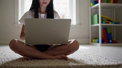 Aufkleber - Comfortable pupil sitting cross legged on a carpet, using a laptop in their bedroom for online education, with a bookshelf visible in the background