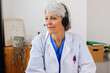 © Xavier Lorenzo - Senior doctor in white coat and headset working on laptop at office desk. Professional practitioner woman typing on keyboard looking at computer screen at clinic workplace. Healthcare people concept.