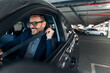 © Jelena - Man Smiling and Buckling Seatbelt Inside Car at Urban Parking Garage
