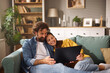 © Stockphotodirectors - Two people sitting closely on a couch in a warm, inviting living room, sharing a joyful moment as they look at a laptop together during a relaxing evening.