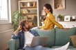 © Stockphotodirectors - Two people relax in a comfortable living room. One is sitting on a sofa with a laptop, while the other stands nearby holding a coffee cup and engaging in conversation.