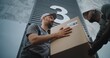 © Framestock - Outside of Logistics Retail Warehouse: Employee Taking Cardboard Box with Online Orders and E-Commerce Goods from African American Worker of Express Delivery Service. Low Angle Shot. Slow Motion.