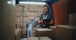© Framestock - Logistics Warehouse: Female Manager with Digital Tablet Scanning Cardboard Boxes Using Barcode Scanner. Diverse Employees Unloading Pallet Truck with Online Orders, Purchases and E-Commerce Goods.