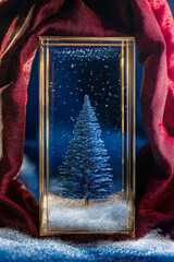 Wall Mural - Small blue tree is in a glass case with snow on the ground. The scene is set in a red background, giving it a festive and cozy atmosphere