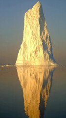 Poster - Iceberg reflecting golden sunlight on calm ocean at sunrise, serene nature scenery