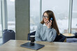 © DSMT - A dedicated young woman, engaged in a crucial phone call, is comfortably seated in her cozy workspace with a breathtaking winter cityscape view that inspires her productivity and focus