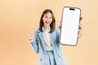 © sitthiphong - Confident Asian businesswoman holding big smartphone mockup of blank screen and smiling on beige color background.