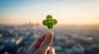 © ManuStockStudio - Close up of a person's hand holding a four leaf clover with a soft focus cityscape background at sunset symbolizing good luck and fortune