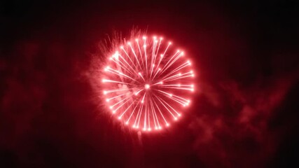 A vibrant red firework bursts and expands across the night sky