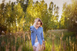 © SergeiPh - A woman is walking through a field of tall grass. She is wearing a blue and white shirt and white underwear. The grass is tall and green, and the sun is shining brightly