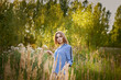 © SergeiPh - A woman is walking through a field of tall grass. She is wearing a blue and white shirt and white underwear. The grass is tall and green, and the sun is shining brightly