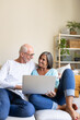 © Daniel - Mature married couple using laptop relaxing on the couch at home living room looking at each other. Vertical image.
