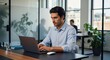 © Havoc - Man in blue shirt typing on laptop in office with window and coworker