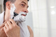 © New Africa - Handsome man shaving with razor at home. Space for text