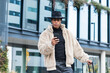 © BUDDHA - Handsome young dark-skinned hipster in hat and winter coat messaging his girlfriend online on smart phone while waiting for her on street, looking at screen