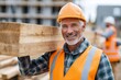 © Lubos Chlubny - Smiling construction worker carrying wooden plank at building site