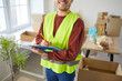 © Studio Romantic - Smiling male volunteer wearing reflective vest holding clipboard and writing notes while working in donation center. Cropped view of happy man organizing food supplies and packing boxes for charity.