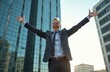 © Vadym - Happy, mature businessman with arms outstretched in front of modern office building. Ecstatic male celebrates success. Joyful man with gray hair in suit enjoying freedom after work outdoors.