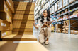 © TeTe Song - Focused on her task, young asian woman sitting and holding clipboard meticulously updates inventory records while surrounded by shelves filled with various products in a vibrant warehouse setting