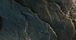 © dkalashnikov - Close-up of cracked dark rock surface with soft lighting and layered texture