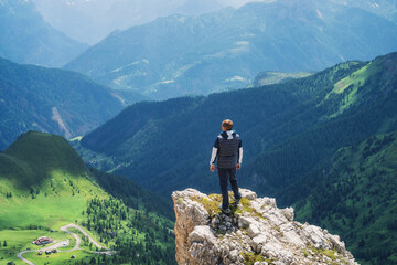 Wall Mural - man hiker standing on a cliff is enjoying the breathtaking view of the surrounding mountain range, g