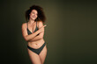 © deagreez - Confident Young Woman Embracing Natural Beauty in Stylish Dark Green Lingerie Against a Solid Colored Studio Background