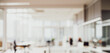 © birulaut - Blurred office space with desks chairs computers and large windows with natural light.