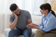 © New Africa - Psychologist supporting patient during therapy session on sofa in office