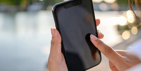 Woman using smartphone with blank screen near lake at sunset