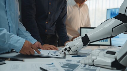 Poster - A modern office scene shows a robot arm assisting humans in data analysis, emphasizing teamwork and the integration of technology in professional environments.Noogenesis