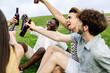 © Xavier Lorenzo - Young group of diverse friends having fun drinking beer during summer vacation, relaxing together sitting on grass at city park