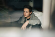 © Maskot - Thoughtful young man looking away while sitting near bed at home